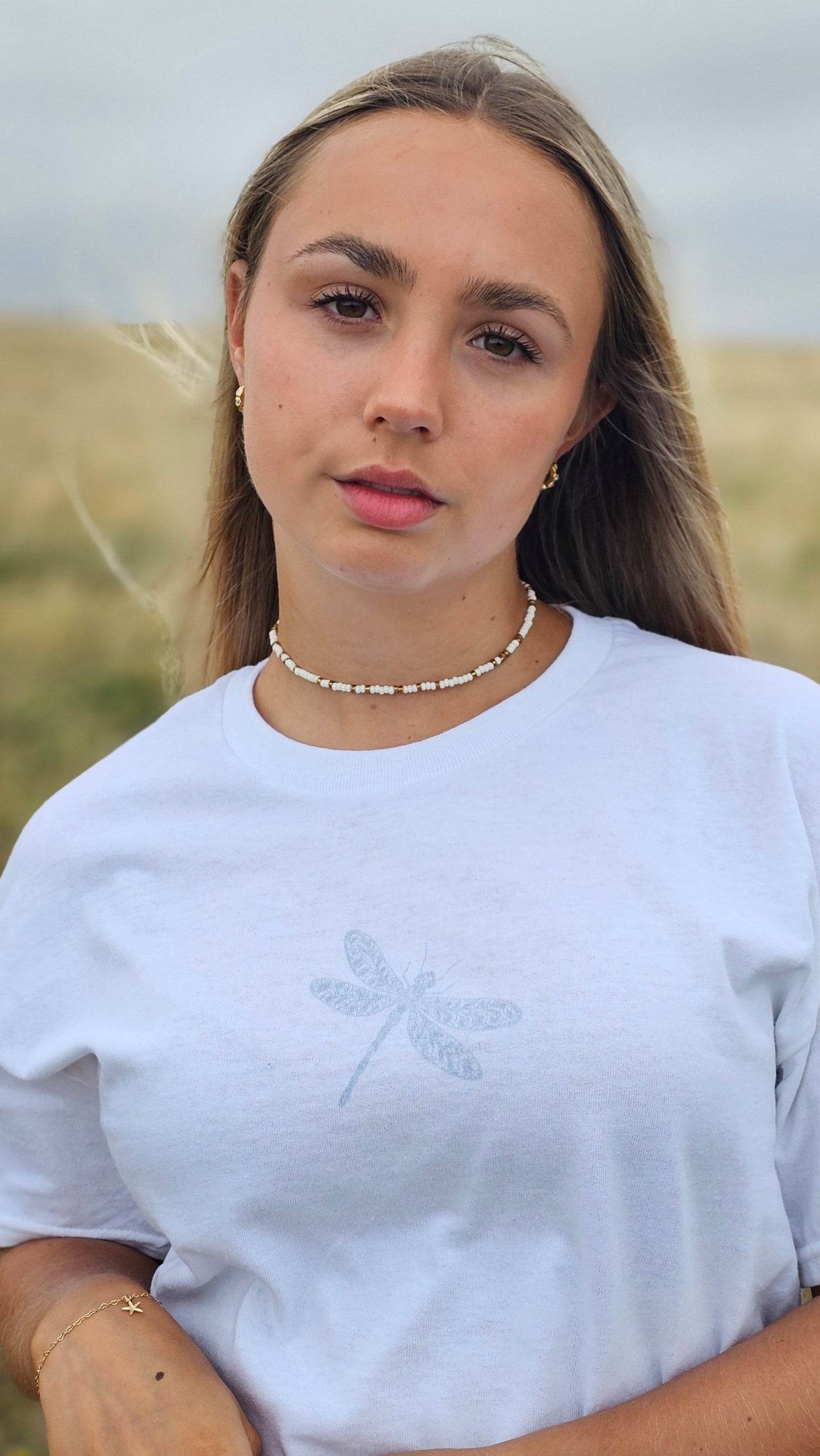 Woman wearing a white shirt with a subtle design, standing against a neutral background.