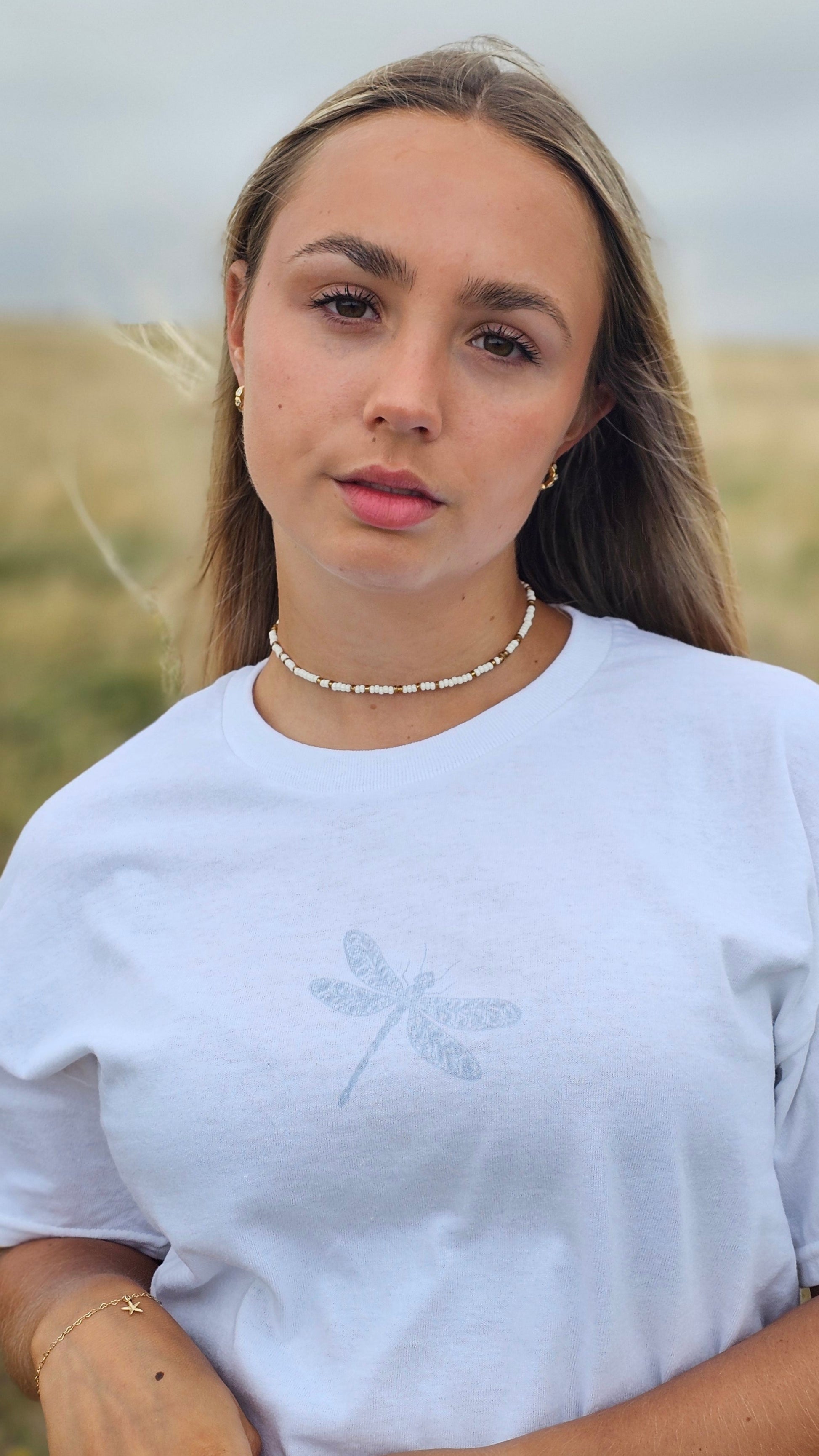 Woman wearing a white shirt with a subtle design, standing against a neutral background.